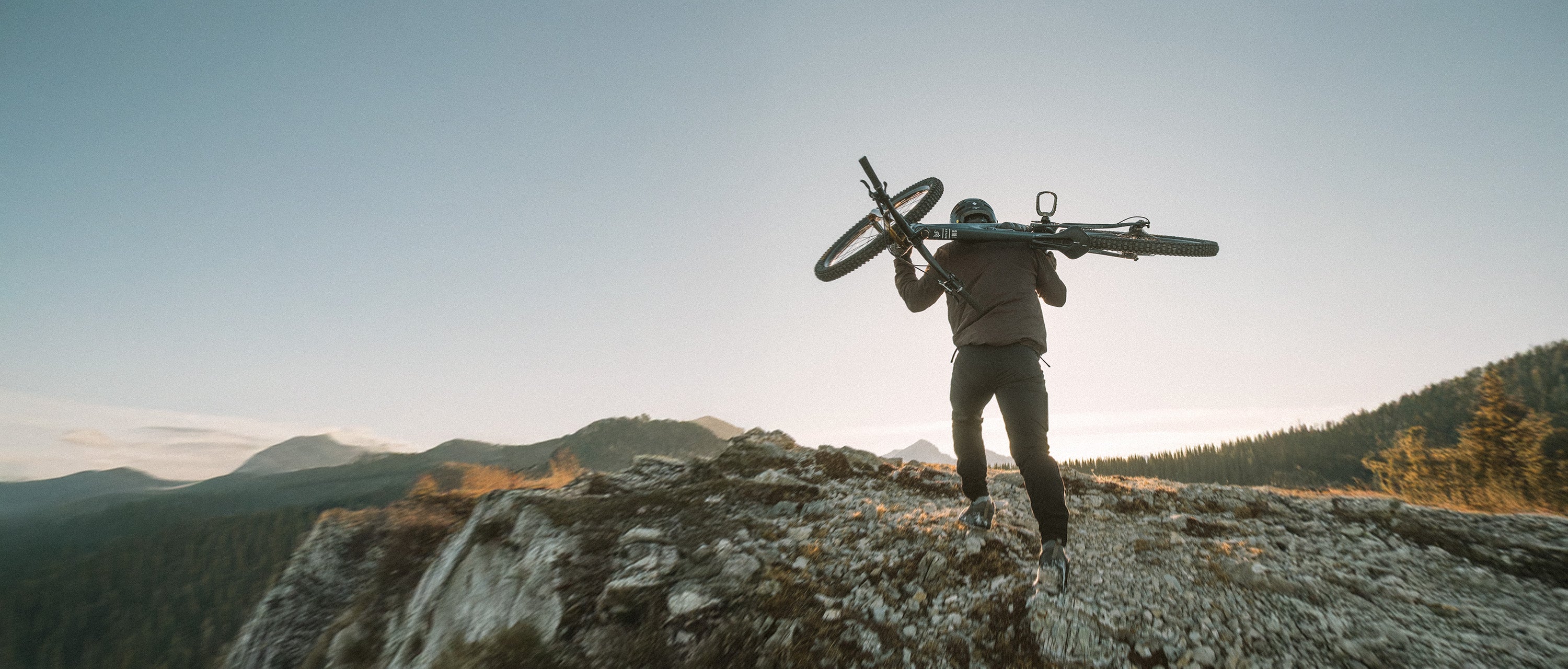 Mountain biker carrying a mountain bike along a rocky ridge at sunrise